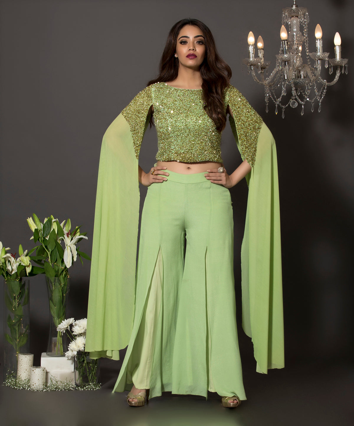 Pista green lycra net cape sleeves georgette blouse with pearls and sequins embroidery paired with front slit palazzos made out of pure crepe.