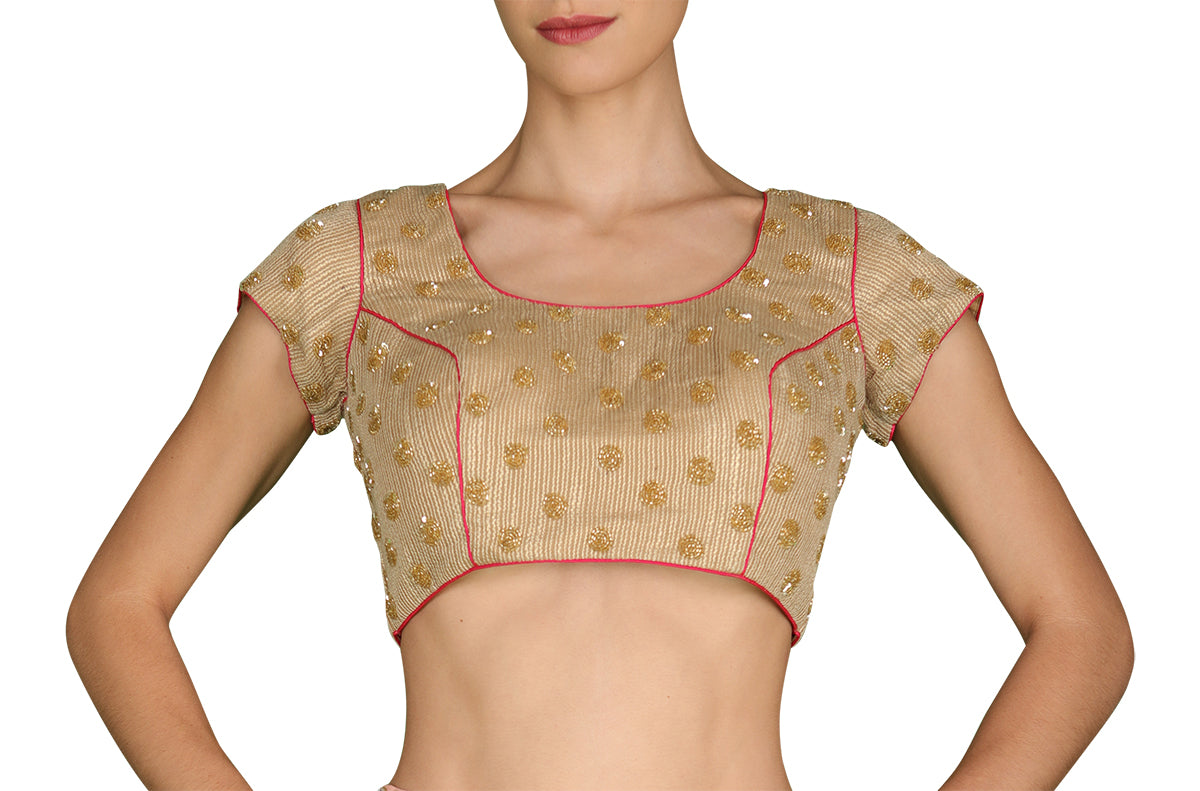 Raise the temperature in this light gold textured blouse highlighted with gold hand embroidered round motifs and dark pink piping.